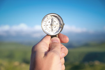 Man searching direction with a compass in his hand in the summer mountains point of view. Direction Search