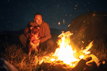 A man and his dog next to a campfire at night