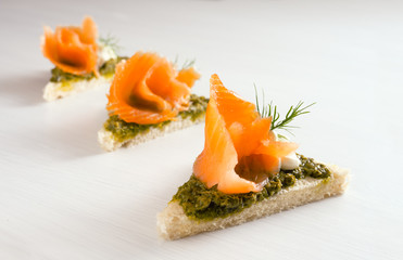three canapes in a row with smoked salmon, pesto, cream and dill garnish on a light background with copy space