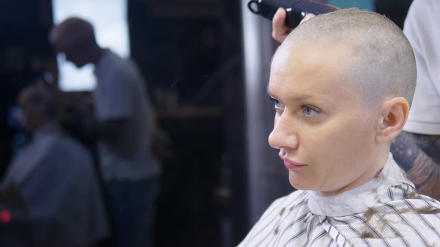 concept of hair loss after chemotherapy. the hairdresser shaves the rest of the hair on the head of a bald woman who survived after chemotherapy. hope for survival.