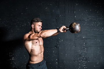 Young strong sweaty focused fit muscular man with big muscles holding heavy kettle bell for swing cross training hard core workout in the gym