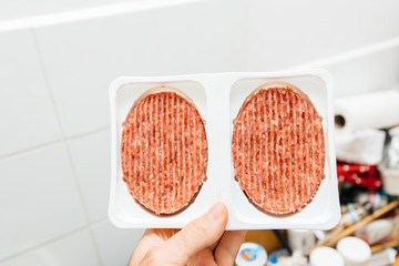 man hand holding fresh steak cutlets in white plastic recipients against white kitchen environment