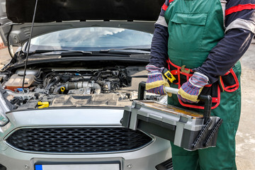 Mechanic in uniform posing with tool box near car engine