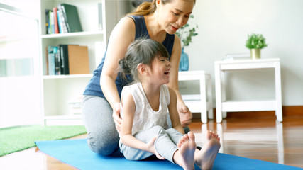 Asian mother teaching her daughter and practicing light yoga exercise stretching movements on a mat learning to control various parts of the body in the brightly lit sunny morning living room. Concept