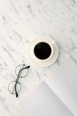 Flat lay vertical mockup hipster glasses, coffee cup and opened blank magazine with copy space on marble background