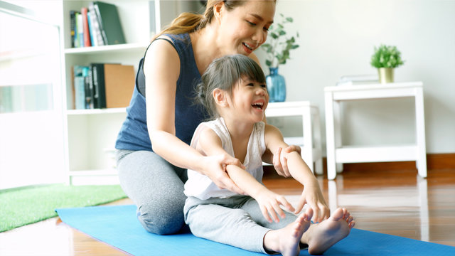 Asian mother teaching her daughter and practicing light yoga exercise stretching movements on a mat learning to control various parts of the body in the brightly lit sunny morning living room. Concept
