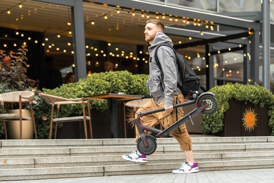 Man holding electric kick scooter while going for a walk at street or at cafe.
