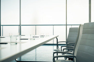 Close up of conference table ready for meeting with glasses, pens and blank sheets in light rroom.