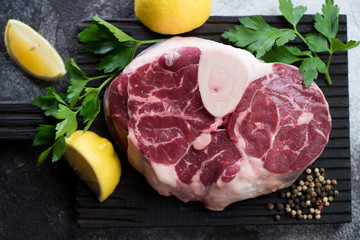 Top view of raw cross cut veal shank with parsley and lemon for making osso buco, close-up