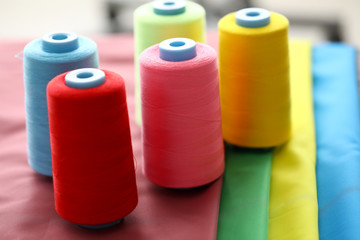 Focus on multicolored spools of strings on fabric swatches. Bobbins in red, blue, pink, yellow and green colors. Fashioner market concept. Blurred background