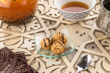 Tasty profiteroles with cream and chocolate glaze and cup of black tea on oriental wooden table
