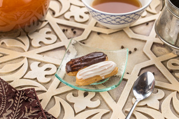 Homemade eclair dessert with chocolate and vanilla sauce and cup of tea on oriental wooden table