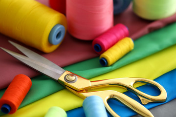 Close-up of sewing equipment for creating fashionable clothes. Professional scissors lying on table covered with diverse strips colorful spools. Fashioner market concept