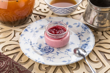Strawberry jam in a jar and cup of black tea on oriental wooden table