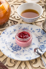 Strawberry jam in a jar and cup of black tea on oriental wooden table