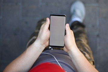 Top view of modern smartphone in male hands. Man in casual clothes holding stylish mobile phone. Empty copy space on gadget display. Blurred background