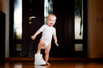 A child playing trying on a big sneaker of a father, standing in the corridor.