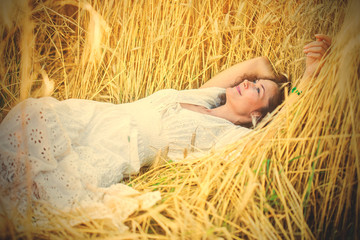 smiling woman in white dress lying among the ears of wheat