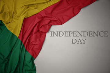 waving colorful national flag of benin on a gray background with text independence day.