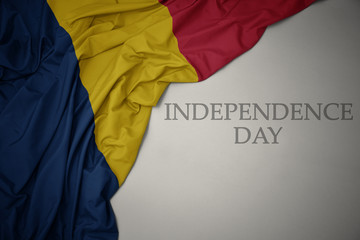 waving colorful national flag of chad on a gray background with text independence day.