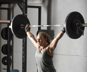 Close up of strong young woman lifting barbell over her head in gym.