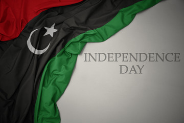 waving colorful national flag of libya on a gray background with text independence day. - obrazy, fototapety, plakaty