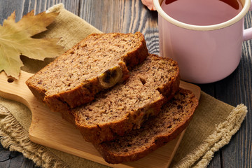 Autumn food-slices of banana bread, a Cup of tea, dry leaves, a dark wooden table. Side view.