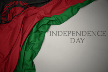 waving colorful national flag of malawi on a gray background with text independence day.