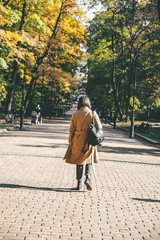 woman in coat with backpack walking by autumn city park