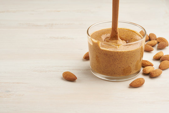 almond butter, raw food paste made from grinding almonds into nut butter, crunchy and stir, white wooden table, copy space