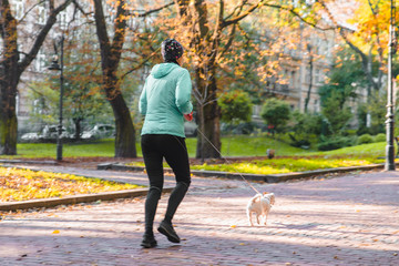 Fototapeta premium woman running with dog on leash at autumn city park