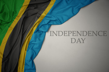 waving colorful national flag of tanzania on a gray background with text independence day.