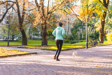 woman running with dog on leash at autumn city park