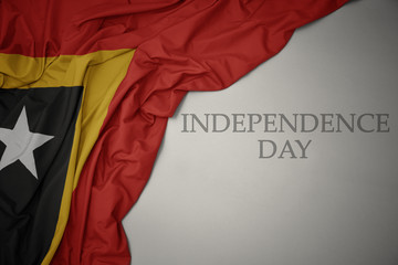 waving colorful national flag of east timor on a gray background with text independence day.