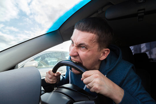 An unbalanced, goosey man bites a car steering wheel from anger while driving in a traffic jam or after an accident. A nervous and nutty guy cannot restrain his emotions and yells at other road users.