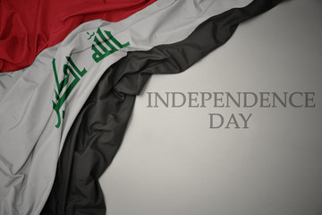 waving colorful national flag of iraq on a gray background with text independence day. - obrazy, fototapety, plakaty