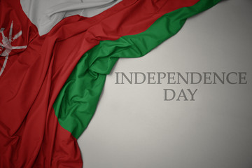 waving colorful national flag of oman on a gray background with text independence day.