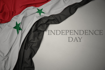 waving colorful national flag of syria on a gray background with text independence day.
