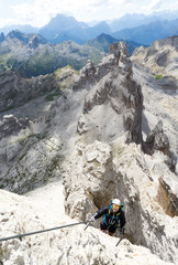 young male mountain climber on a steep and exposed rock face climbing a Via Ferrata