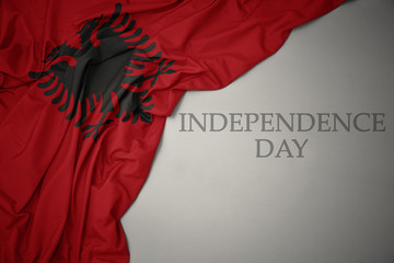 waving colorful national flag of albania on a gray background with text independence day. - obrazy, fototapety, plakaty