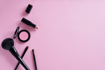 Flat lay composition of decorative cosmetics, different makeup brushes, blush, lipstick on a pink background. Top view. Minimalistic lifestyle.