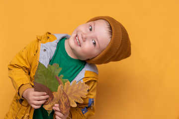 Autumn time. Smiling baby with yellow leaves in hand. Seasonal fashion. Autumn clothing. kids fashion. Leaf fall. boy in golden clother, orange hat