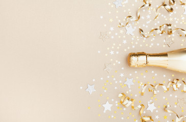 Golden champagne bottle with confetti stars and party streamers top view. Christmas, birthday or wedding background. Flat lay style. © juliasudnitskaya