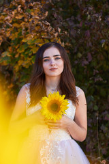 Beautiful lovely girl in a white dress with a sunflower in her hands. Sunlight plays on the field. Enjoy the nature. Autumn time.