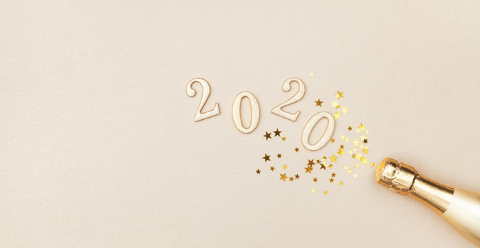Creative Christmas and New Year greeting card with golden champagne bottle, confetti stars and 2020 numbers. Flat lay. Banner format.