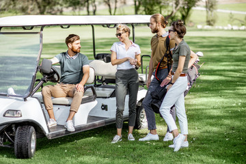 Group of a young friends hanging out together with golf equipment near the golf car on the playing...