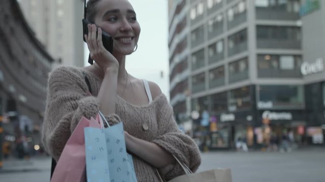 A young woman with multiple shopping bags talking on the phone.