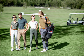 Young and elegant friends walking with golf equipment, hanging out together on the beautiful course with golf car on the background