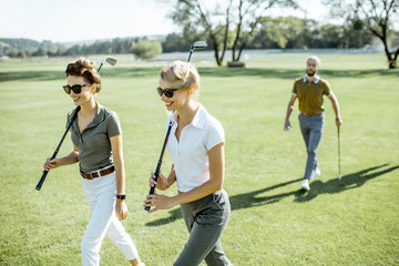 Two female best friends walking together with playing putters during a golf game on a course on a...