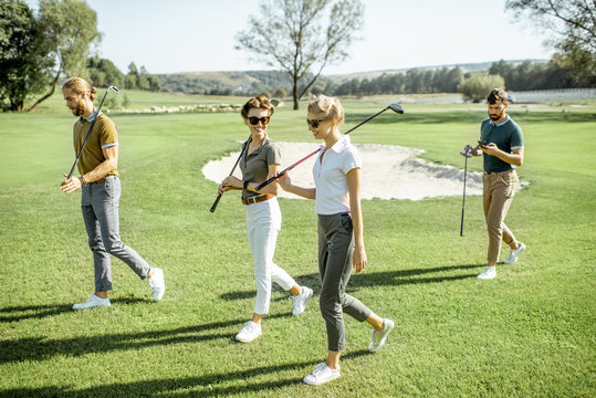 Young friends dressed casually walking with putters on the golf course during a game on a sunny day